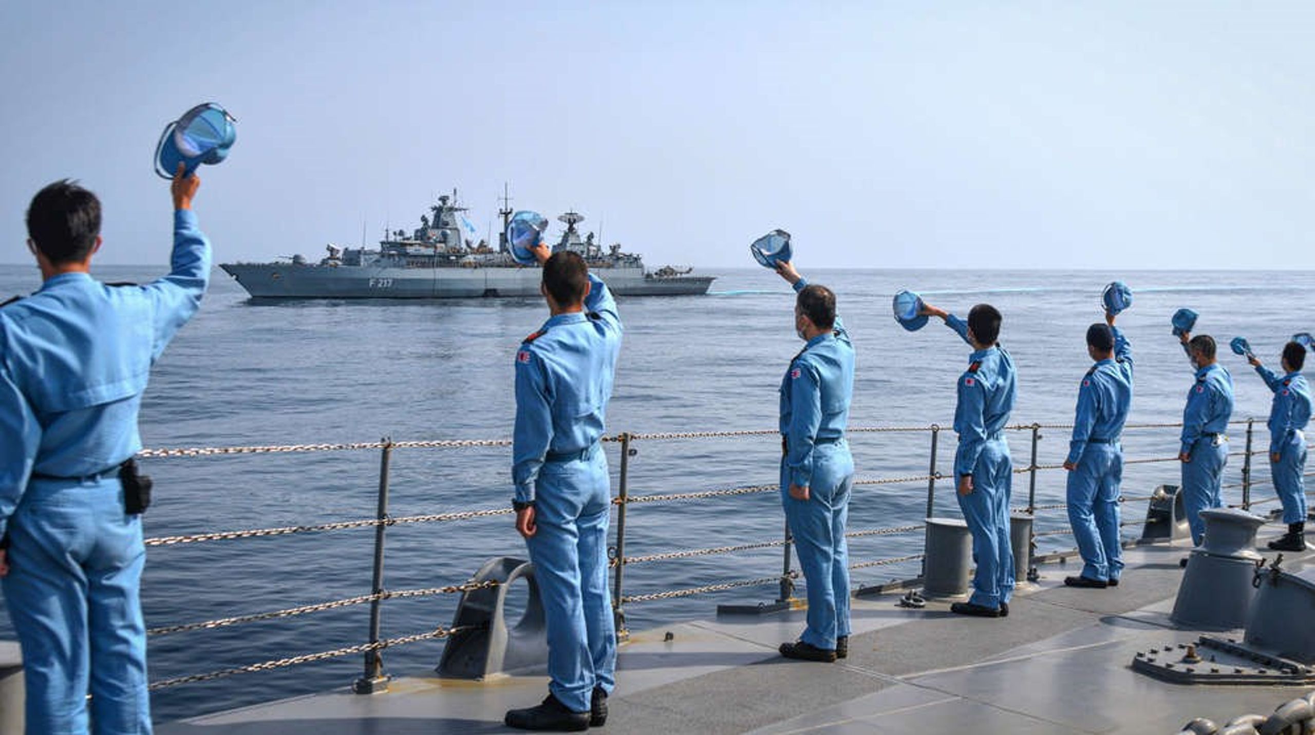 Søfolk på den japanske destroyer Yuugiri hilser på den tyske fregat Bayern syd for Japan.